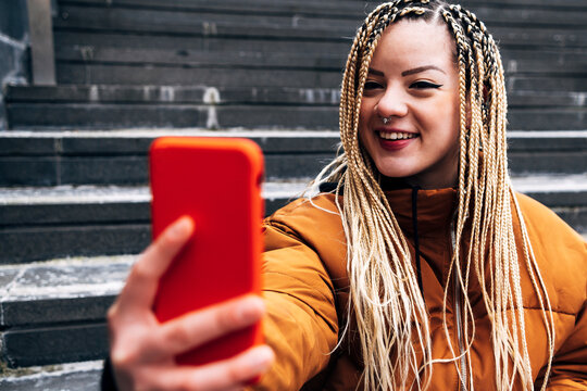 Young smiling woman taking selfie through mobile phone while sitting on steps