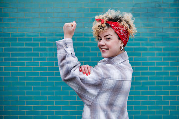 Smiling curly haired woman in bandana flexing muscles