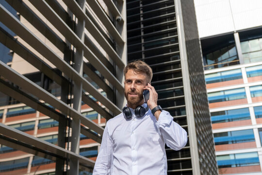 Mid adult businessman with headphones talking on mobile phone while standing in city