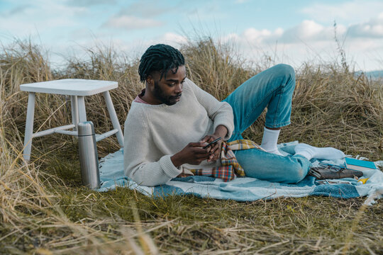 Young man using mobile while lying on blanket at beach
