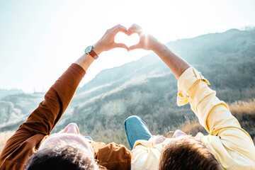 Gay couple doing heart shape with hands in front of mountain