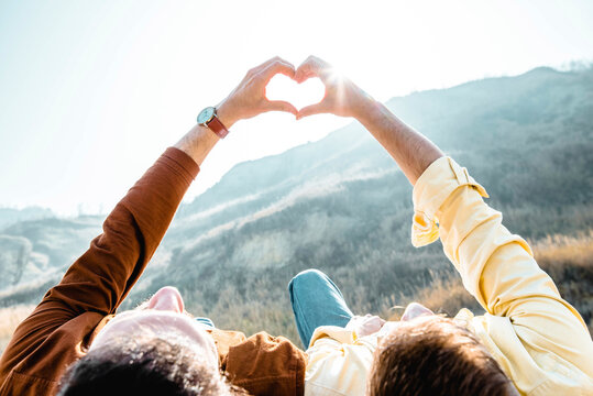 Gay couple doing heart shape with hands in front of mountain