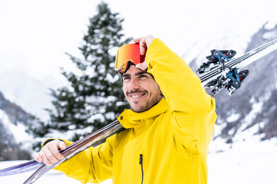 Smiling man with ski looking away while standing on snow covered valley