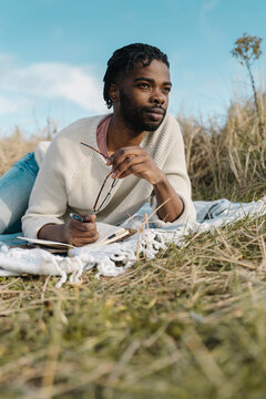Young man with diary lying on blanket amidst dried plants looking away