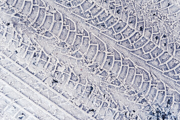 Diagonal traces of car tires in the fresh snow on the asphalt. Close up view from above