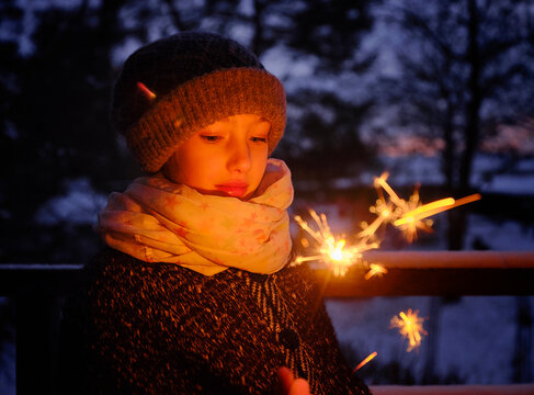 Girl in warm clothing with sparkler at dusk during winter