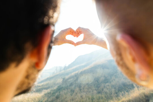 Gay couple doing heart shape with hands at beach