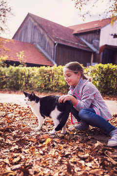 Girl playing with cat while crouching on dry leaf path
