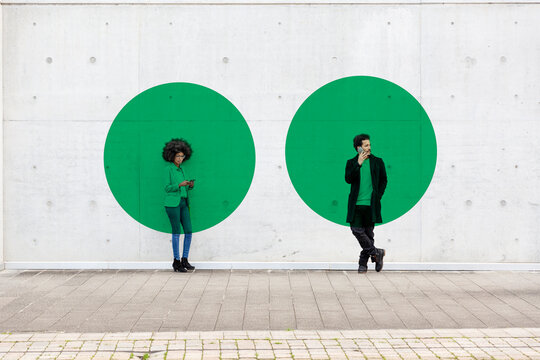 Two circles visualizing social distancing covering man and woman standing outdoors with smart phones in hands