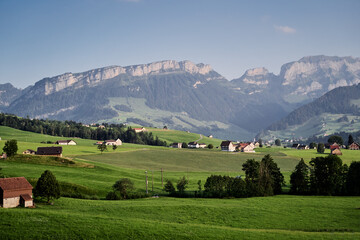 Fototapeta na wymiar Beautiful summer landscape with houses on green field, Swiss Alps Mountains.