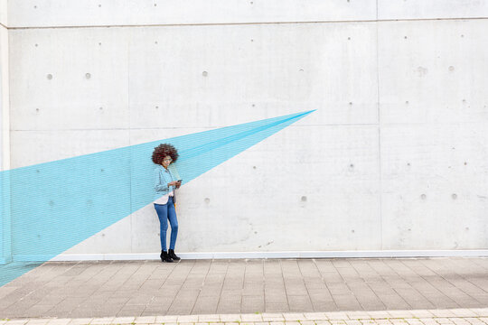 Young woman standing outdoors with smart phone in hands covered in blue facial recognition effect