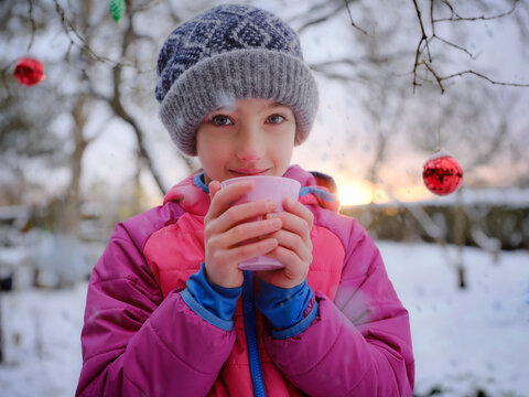 Cute girl in warm clothing with tea cup against Christmas decoration during winter