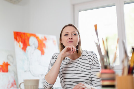 Thoughtful woman with pen sitting at home studio