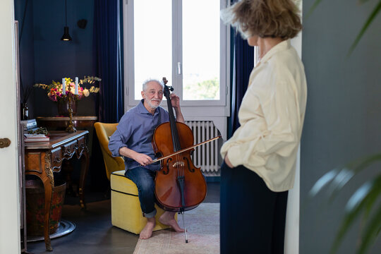 Smiling man looking at woman while playing cello at home