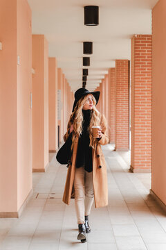 Young woman with reusable coffee cup walking through corridor