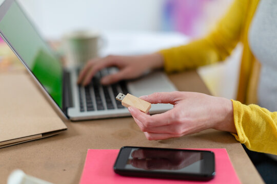 Woman holding USB stick by laptop and mobile phone on table at home