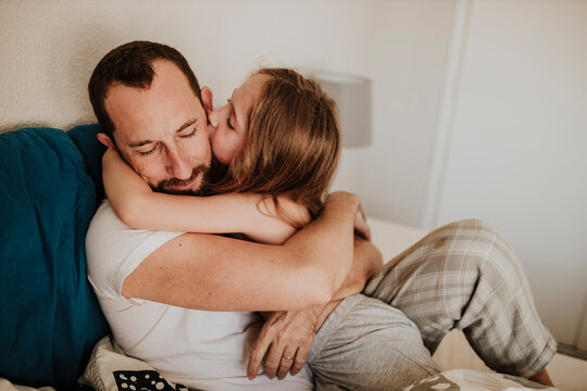Daughter kissing father on cheek while hugging on bed at home