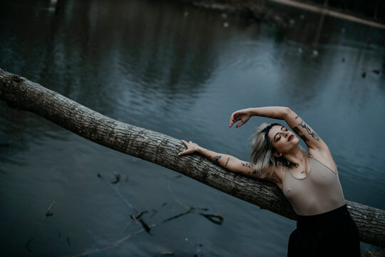 Tattooed young woman leaning on fallen tree against lake