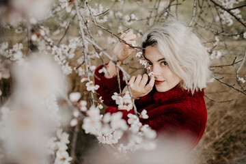 Blond woman touching branch while standing below blossoming almond tree