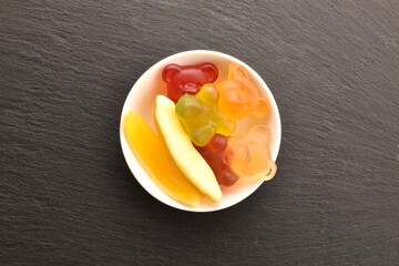 Several sweet jelly candies in a white ceramic saucer on a serving slate board, close-up, top view.