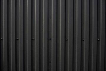 Black corrugated iron sheet used as a facade of a warehouse or factory. Texture of a seamless corrugated zinc sheet metal aluminum facade. Architecture. Metal texture.