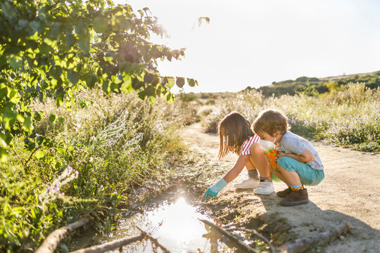 Brother and sister with protective face mask playing at puddle on road during sunny day - Powered by Adobe