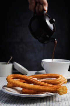 Plate of churros with hand of man pouring hot chocolate in background