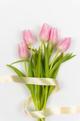 Tenderly pink tulips with ribbon on a white background. Top view. Vertical photo. Valentine's Day. Easter. Mother's day. Spring flowers