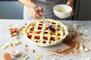 Hands of man applying egg wash to raw strawberry pie