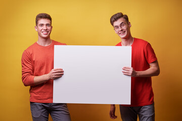 Advertising. Your text here. Couple of handsome young men holding an empty board with copy space...