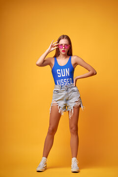 Summer urban fashion. Fun and colorful. Young pretty happy woman in shorts posing against yellow background.