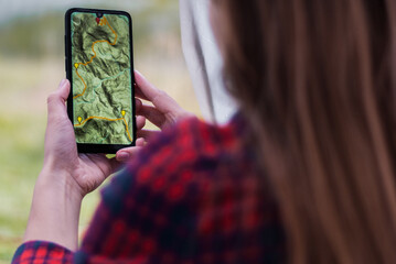 Women hands holding smartphone with app navigation hiking map on screen.  Mountains map with route and markers. Girl planning a trip inside the tent at the camp. 