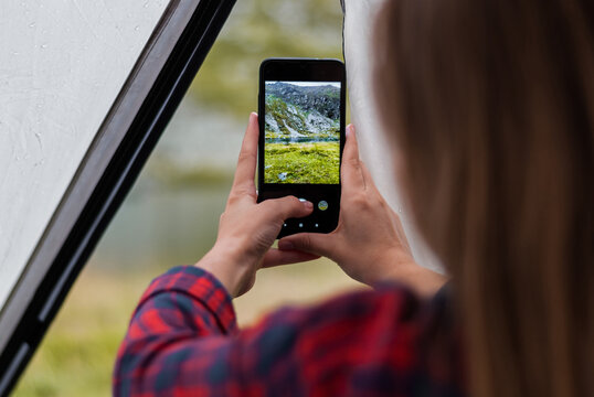 Girl taking photos of the rocky mountains and lake using the phone. Close-up shot of the handі holding the phone. View from the tent.