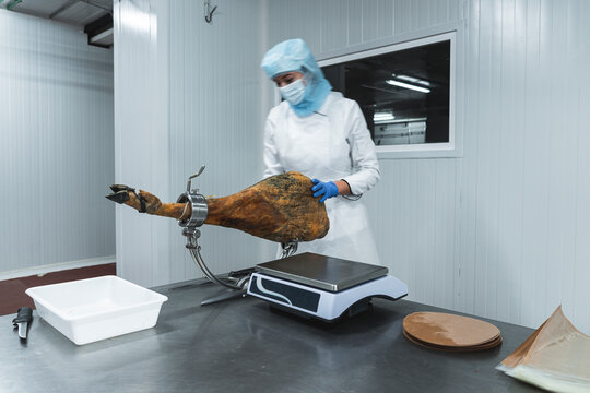 Woman measuring weight of ham leg on scale in factory
