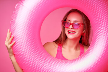 Summer vacation. Studio portrait of pretty young woman holding big pink rubber ring on pink background.