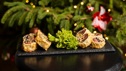 Custom sushi roll in tempura with nori, fresh salmon, tuna, avocado, masago caviar, drizzled with pineapple sauce with salad pouring as decoration on a black plate on a wooden table for Christmas.