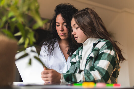 Girl discussing with mother while e-learning through laptop at home