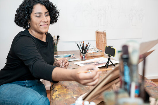 Smiling female painter vlogging through mobile phone at art studio