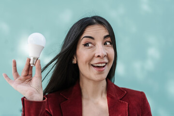 Surprised businesswoman holding light bulb against turquoise wall