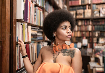 Thoughtful young woman looking away by bookshelf at library