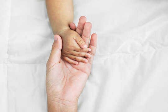 hand of mom and baby on white bed