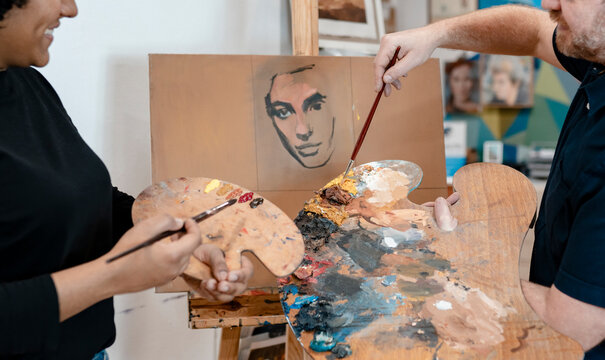 Male artist teaching painting to female painter