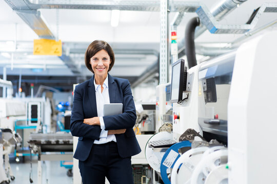Confident businesswoman with digital tablet standing by machinery in factory
