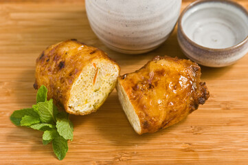 top view, close up of a freshly fried breakfast spring roll, cut in half to see cooked eggs and sake ceramic container and cup with sprig of mint on wood cutting board