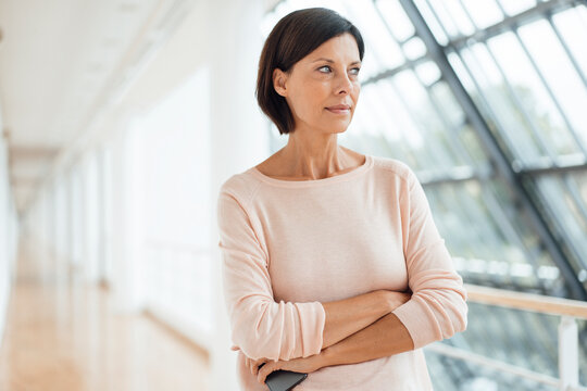 Thoughtful woman with arms crossed looking way at corridor