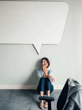 Smiling businesswoman with hand on chin contemplating in office against wall