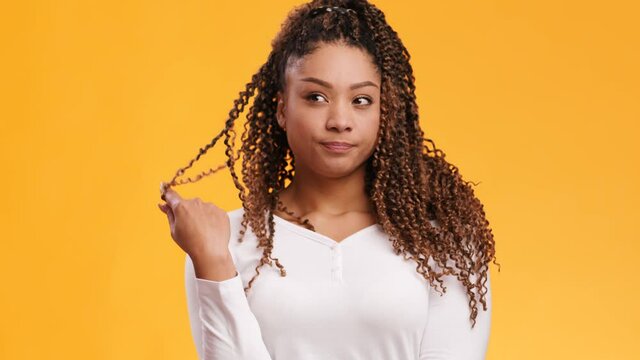 Young pensive african american lady thinking and playing with her braid, orange studio background, slow motion