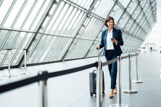 Mature businesswoman with suitcase walking in corridor