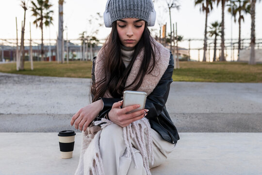Beautiful teenage girl using smart phone while sitting on bench at park