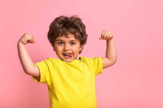Funny little sportive kid boy in yellow shirt, showing his muscles. Happy strong nerd kindergarten child showing bicep. Dream, confidence, success, possible, innovation. Go back elementary school.